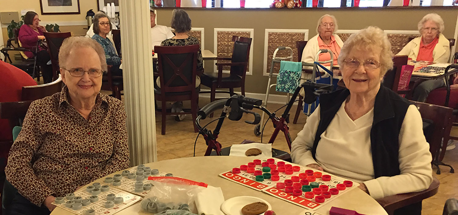 Two Autumn Ridge residents at a bingo card covered in chips, with more players behind them